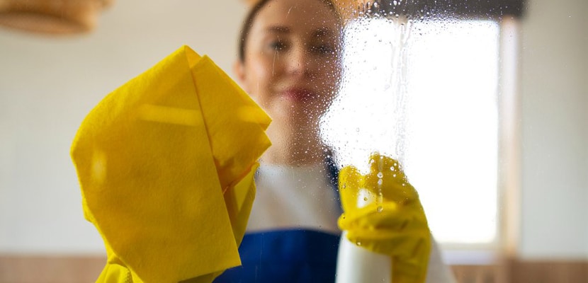 Mujer limpiando vidrios con líquido limpiavidrios y mopa