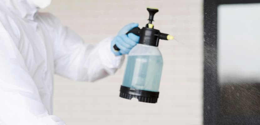 Profesional de limpieza usa protección adecuada mientras esparce limpiador especial sobre una superficie.